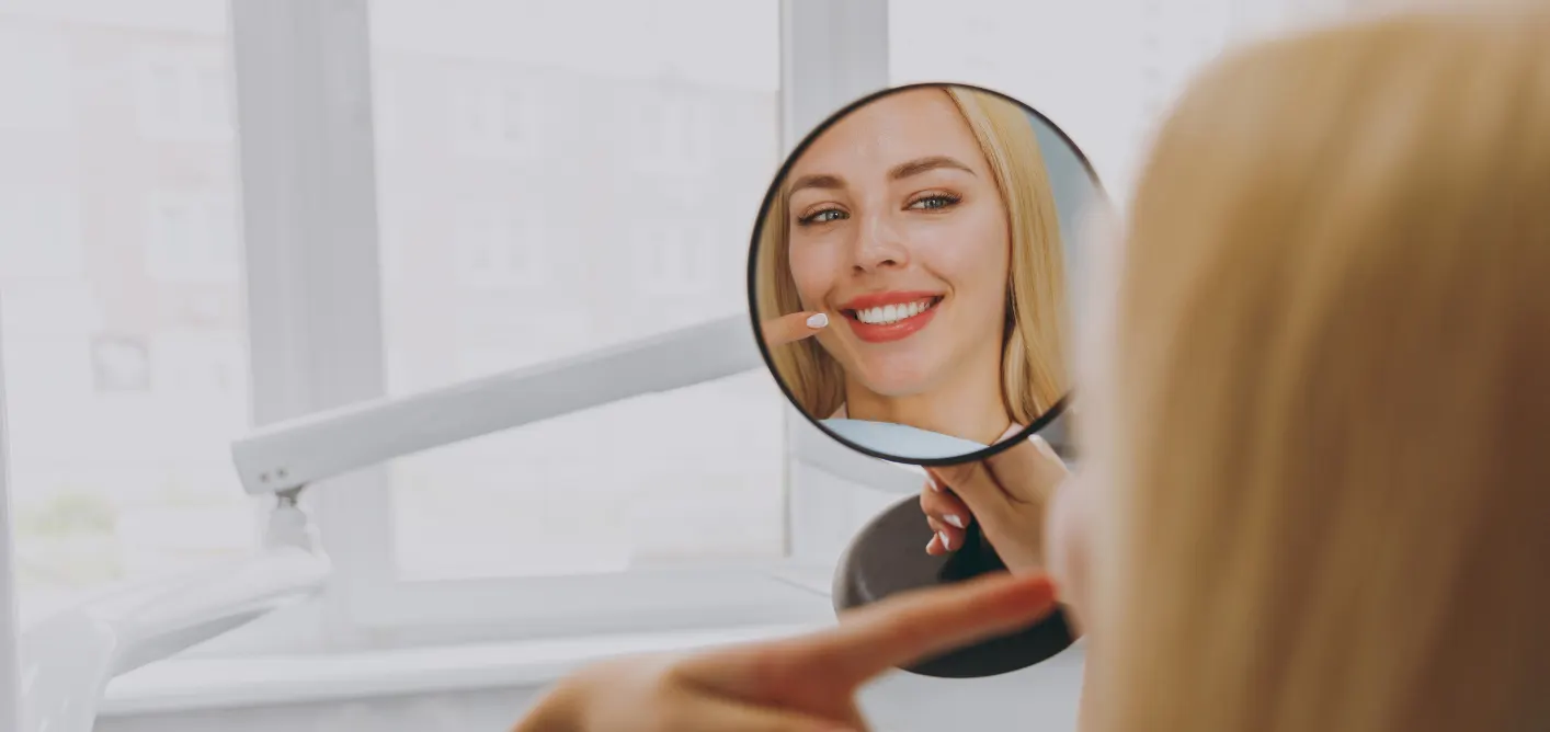 Patient checking her smile in a hand mirror in the dental chair